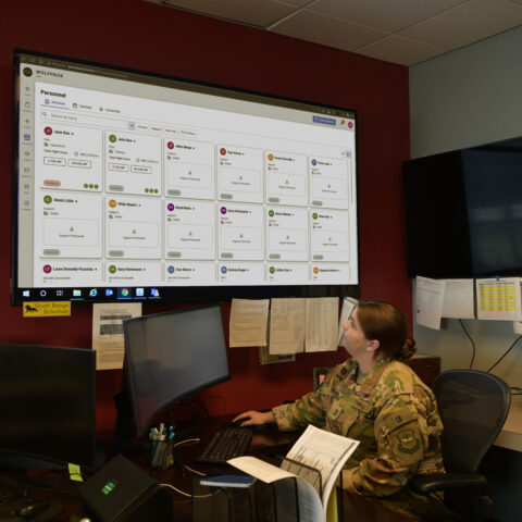 Airman at a workstation with the WOLFPACK readiness dashboard on a wall display